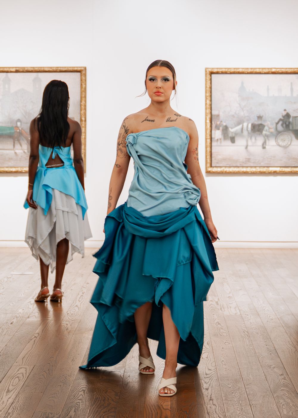 Model in strapless blue ombre ruffled gown walking runway past paintings in art gallery. University fashion show at Manchester art gallery