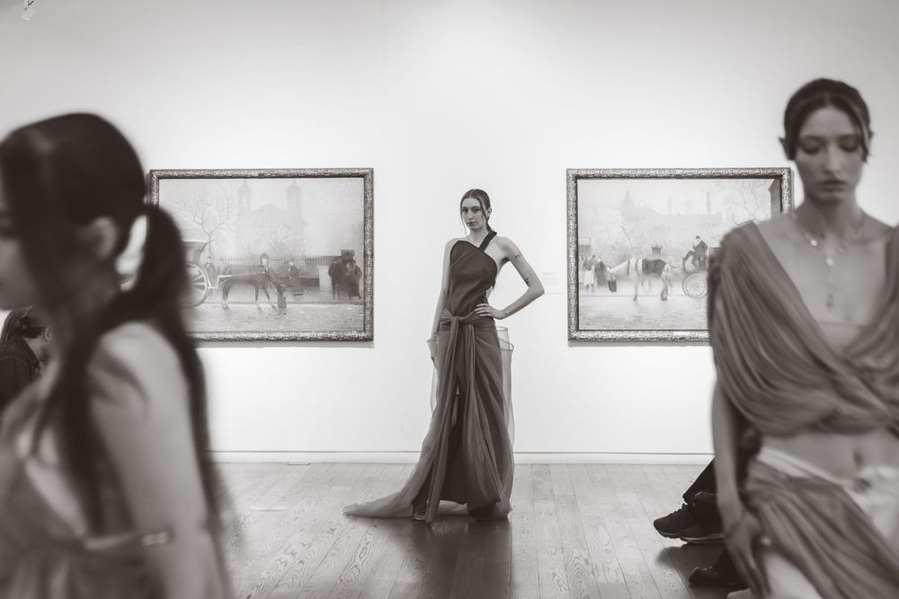 Models pose in draped gowns before classic paintings in black and white gallery shoot. University fashion show at Manchester art gallery