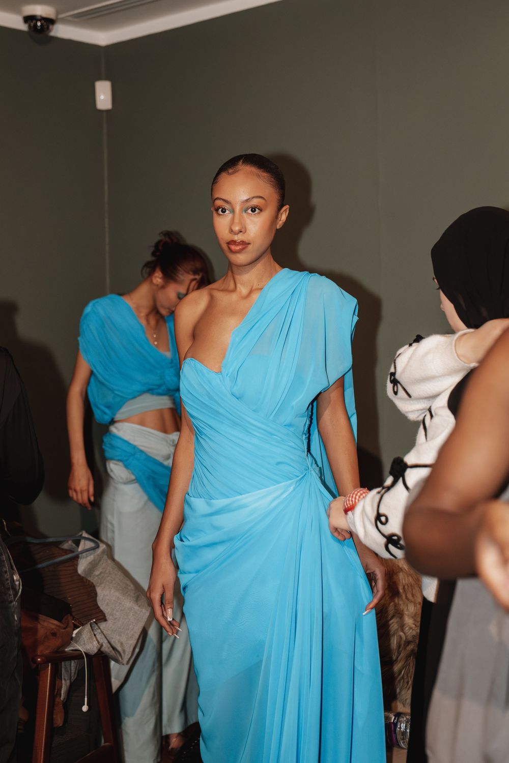 Model in draped turquoise one-shoulder chiffon gown backstage at fashion show. University fashion show at Manchester art gallery
