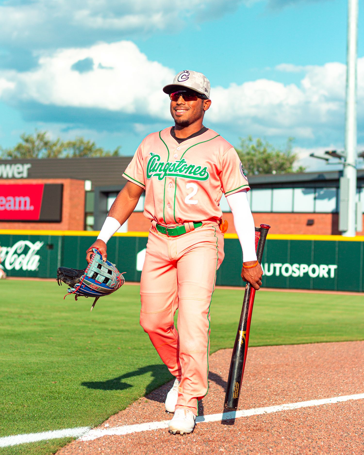 Baseball players in peach-colored uniforms line up along the dugout fence during a sunny day at the ballpark.