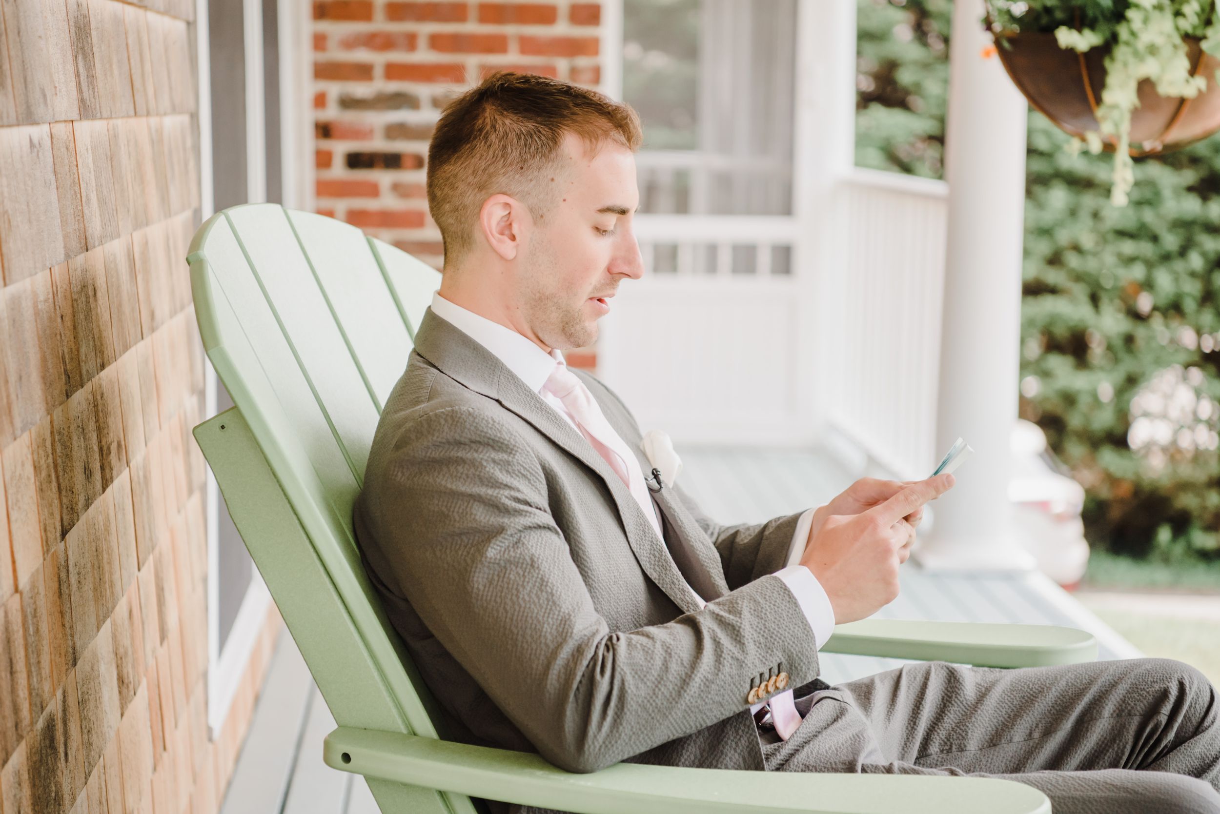 A person in a grey suit relaxes in a mint green Adirondack chair while reading.