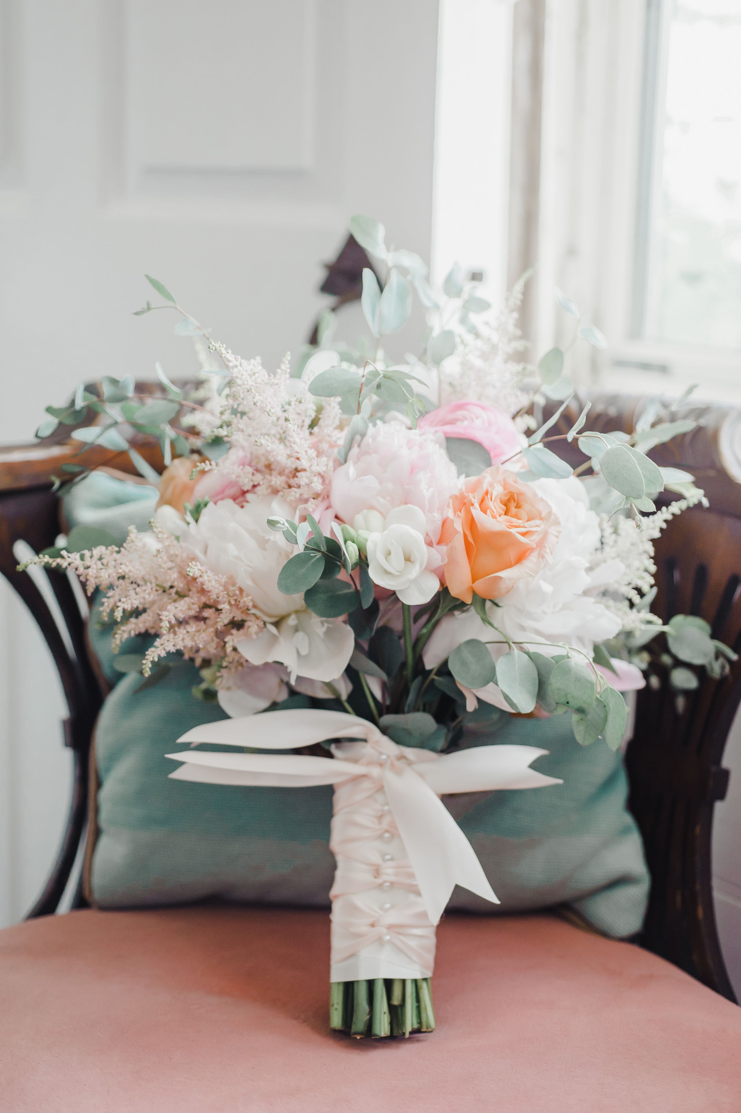 A delicate bridal bouquet featuring pink and peach roses with eucalyptus and white ribbon.