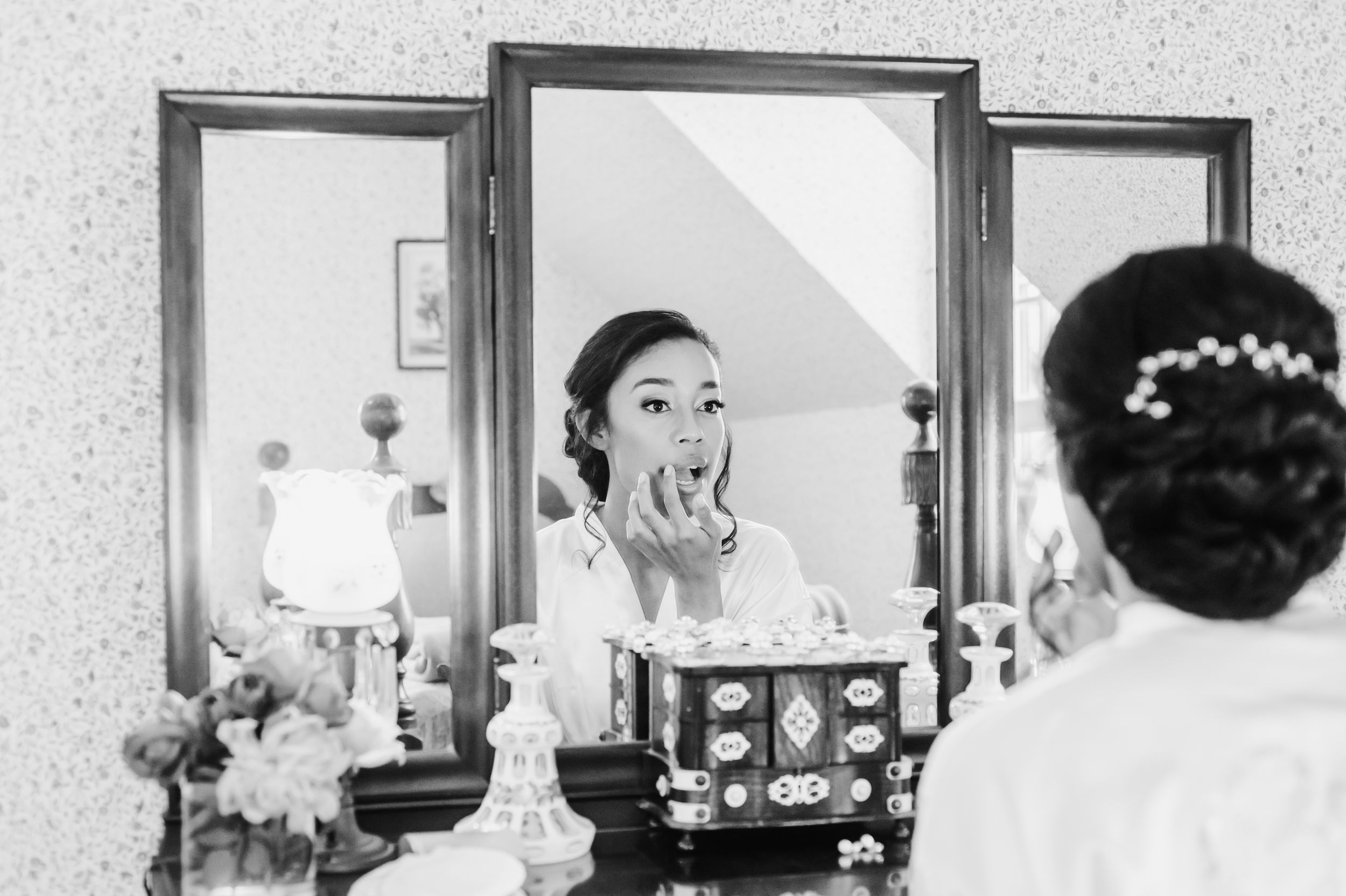 A black and white reflection in a triptych mirror shows preparations with vintage hair accessories and decor.