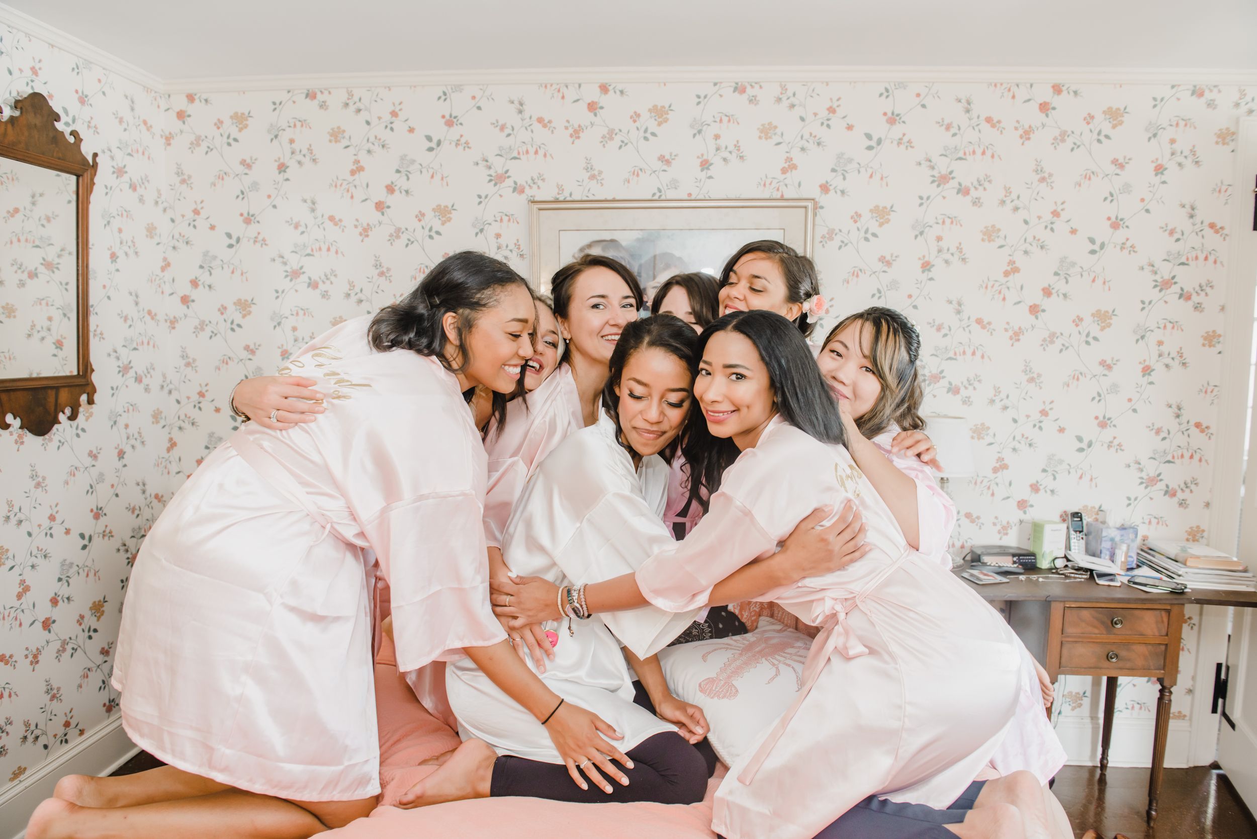 Group in matching pink robes share laughter during wedding preparations.