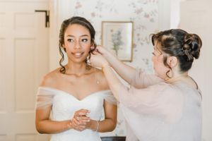 Wedding preparation moment in room with floral wallpaper and natural light.