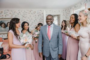 Wedding party gathered in room with floral wallpaper sharing joyful moment together.
