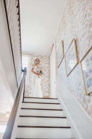 Wedding attire on display at top of staircase with floral wallpaper and gold accents.