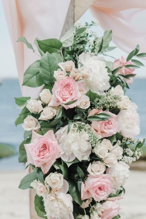 Elegant floral arrangement featuring pink roses, white peonies and greenery against blush fabric backdrop.