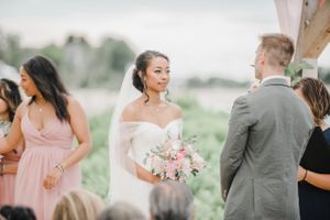 Outdoor wedding ceremony with pink bridesmaid dresses and floral decor against natural backdrop.