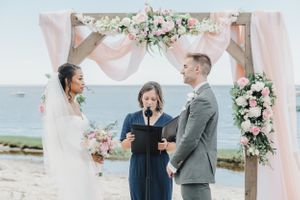 Beachside wedding ceremony under pink floral arch with ocean backdrop.