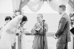 Black and white photo of emotional wedding ceremony moment under floral arch with flowing fabric.