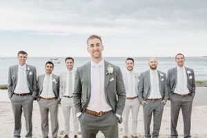 Groomsmen in coordinated gray suits stand together on a beach.