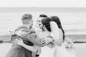 A black and white capture of an emotional group hug during a beach wedding.
