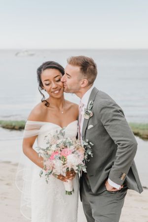 A tender moment between newlyweds with a beautiful pastel flower bouquet on the beach.