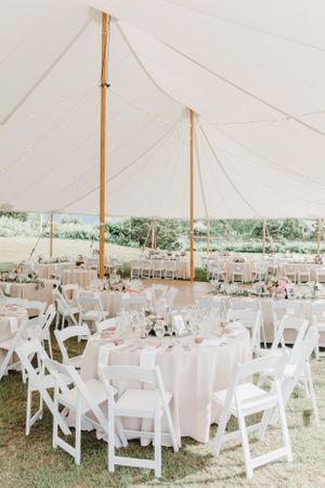 Elegant white tent reception setup with round tables and cross-back chairs.