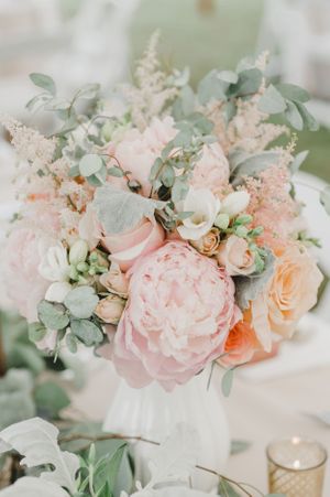 Romantic wedding centerpiece with blush peonies and eucalyptus in soft pastel tones.
