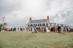 Historic white colonial house with wedding guests gathered on the lawn.