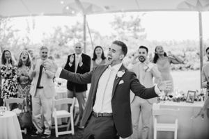Joyful celebration at an outdoor wedding reception under a white tent.