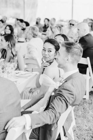 Wedding guests enjoying an outdoor reception at tables under a tent.