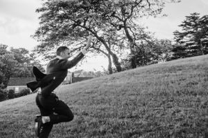 A playful black and white photo of someone leaping on a grassy hillside.