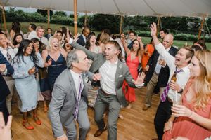 Wedding guests dancing and celebrating on a wooden dance floor under a tent.
