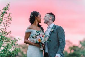 A couple shares an intimate moment against a stunning pink sunset with wedding flowers.