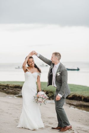 A couple dances together on their wedding day along a coastal path.