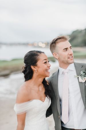 A happy couple share a candid moment on their wedding day by the waterfront.