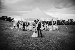 Black and white photo of a wedding celebration under a large tent in an outdoor setting.