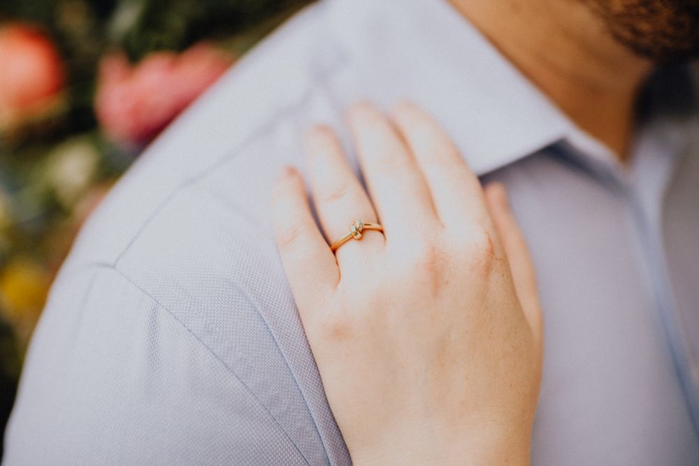 Close-up of hand with engagement ring resting on light blue shirt.
