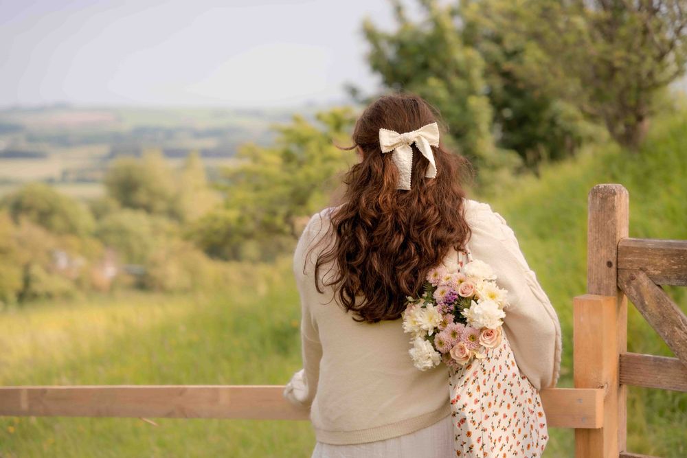 Person in cream sweater holding flowers while looking out over countryside landscape. Lincolnshire branding photographer.