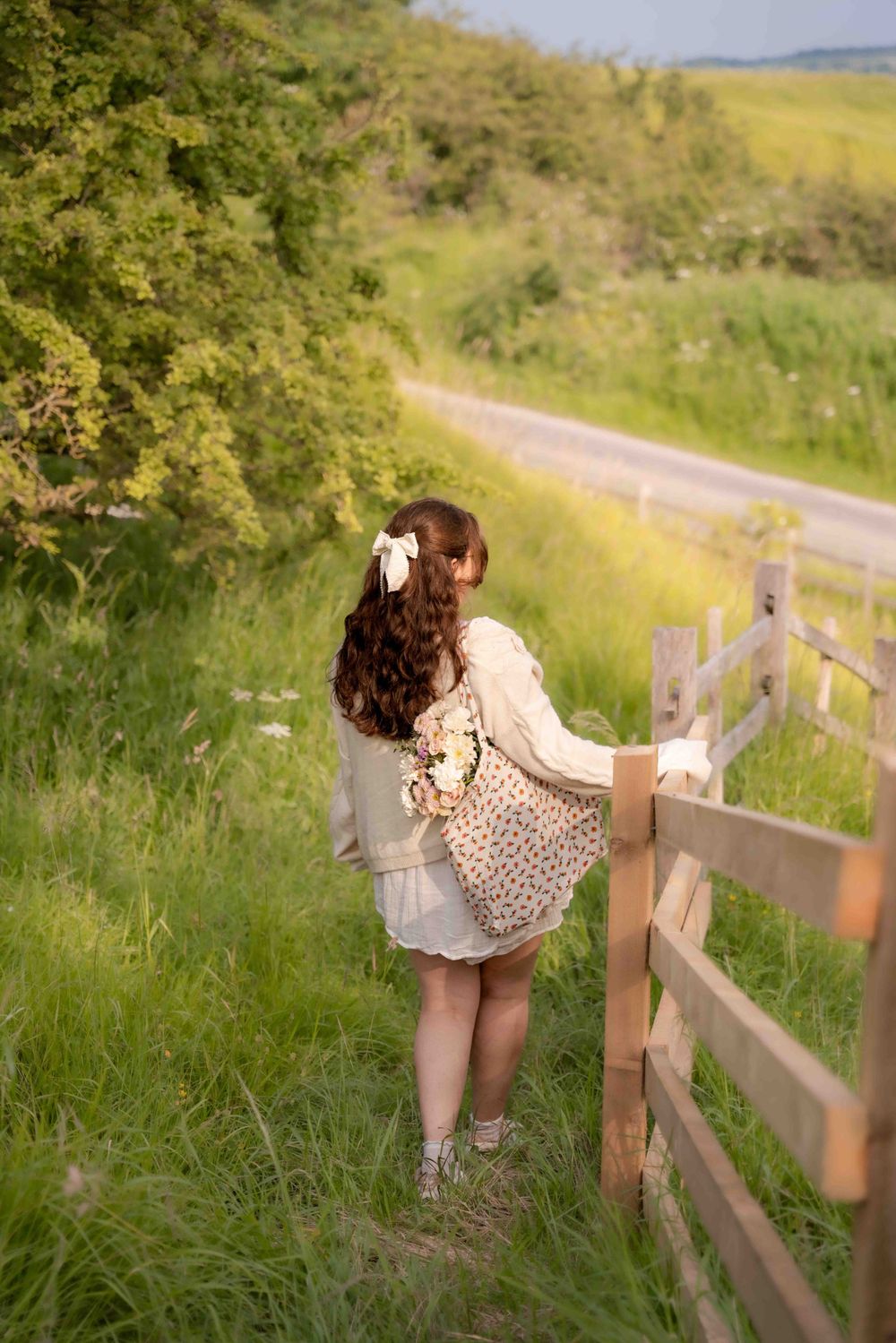 Person in vintage-style dress poses by wooden fence along countryside path. Lincolnshire branding photographer.