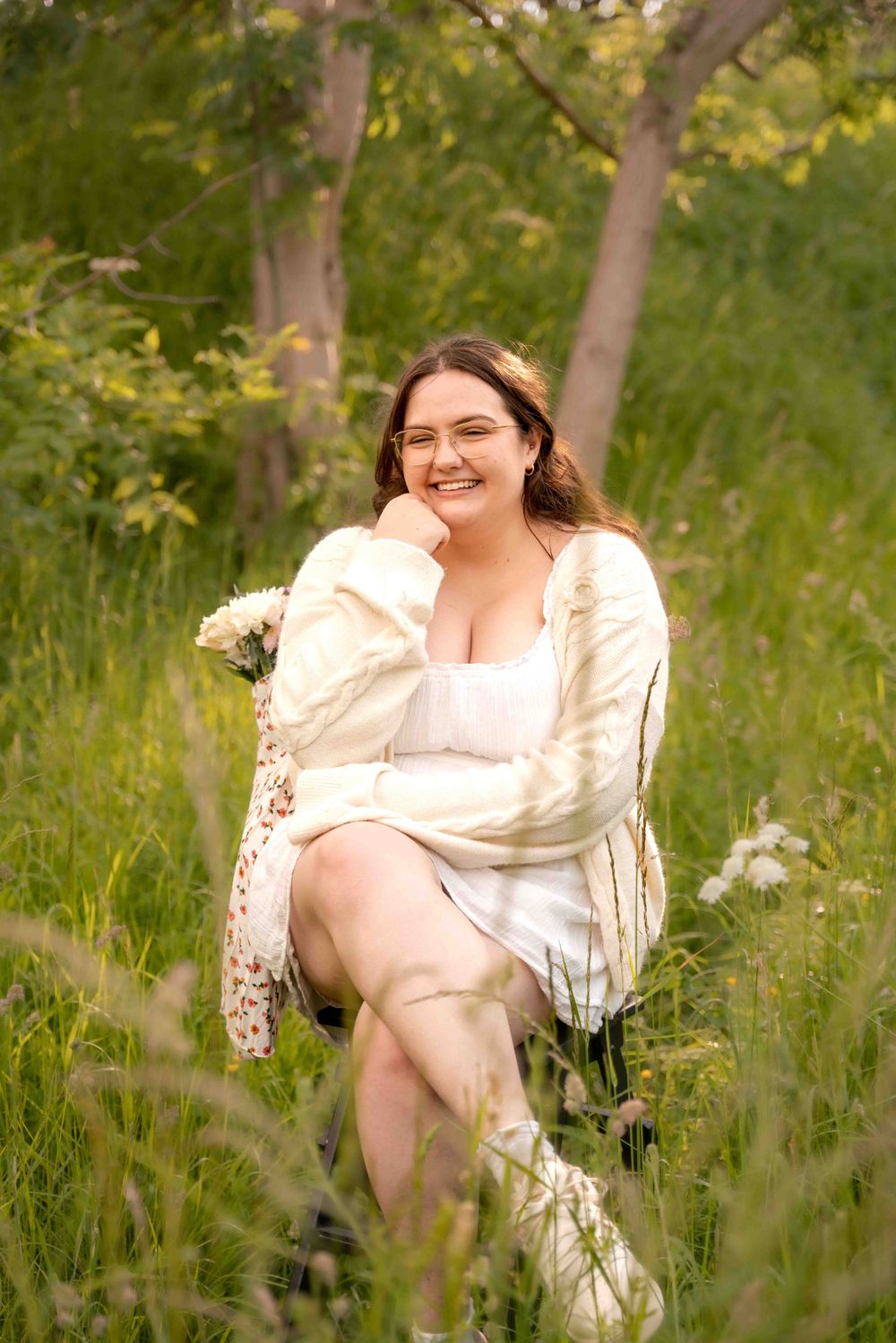 Person in cream dress sitting in tall grass with flowers during golden hour. Lincolnshire branding photographer.
