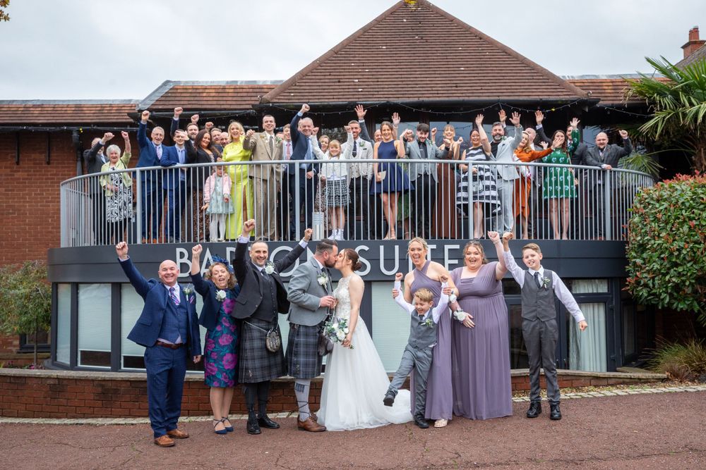 Wedding party and guests celebrating outside the Barco Suite venue with hands raised.