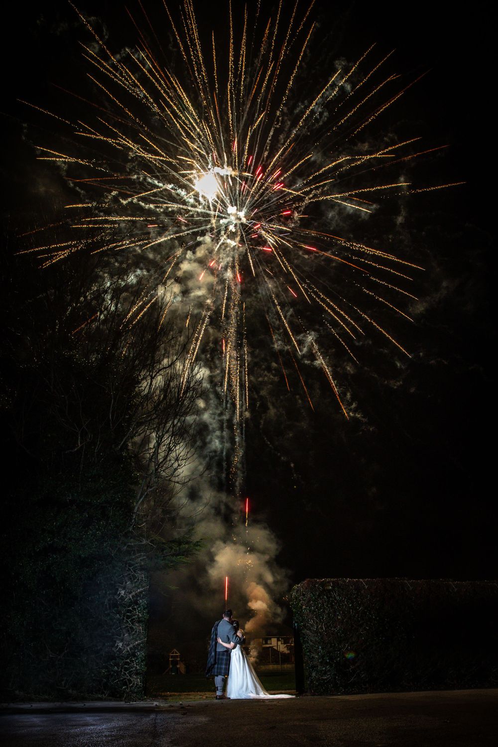 Bride and groom silhouetted against a stunning fireworks display at their evening wedding reception.
