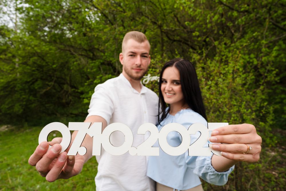 Couple holding date numbers in a green outdoor setting for a save the date photo.