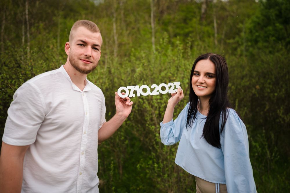 Couple holding numbers for save the date announcement in outdoor setting.