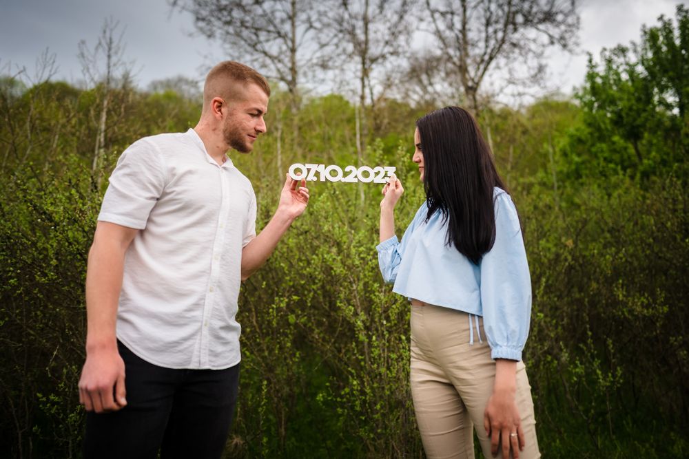 Couple posing with save the date numbers against lush green background.
