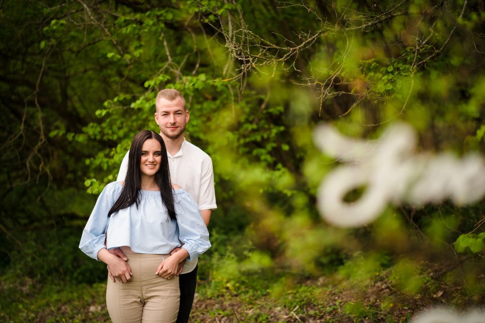 A couple shares intimate moments while posing for photos in a lush green outdoor setting.