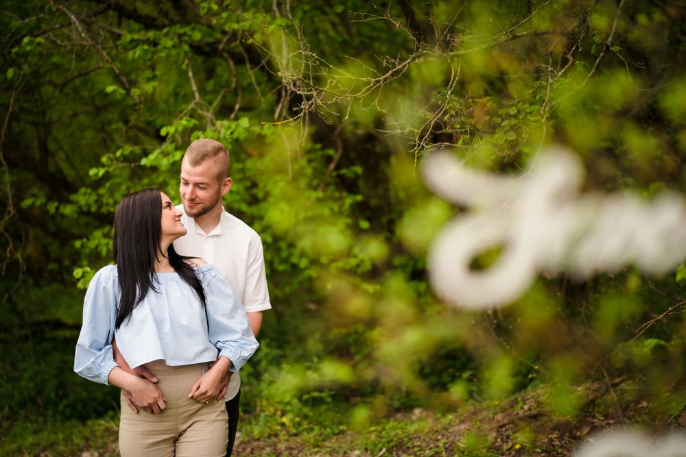 A couple poses together against a backdrop of vibrant green foliage.