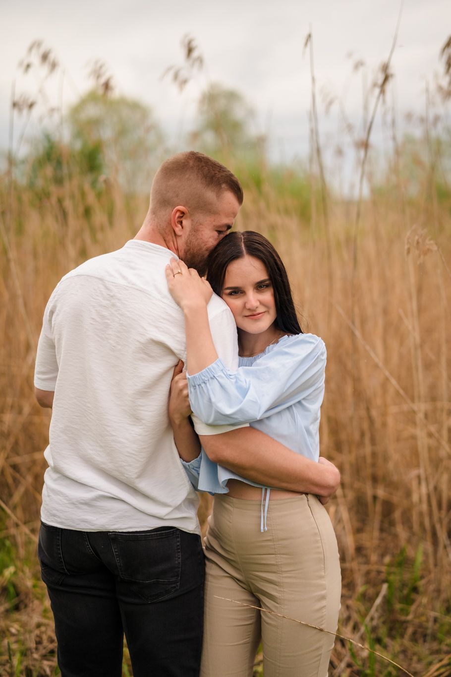 Romantic couple embracing in a field of tall brown grass during golden hour.