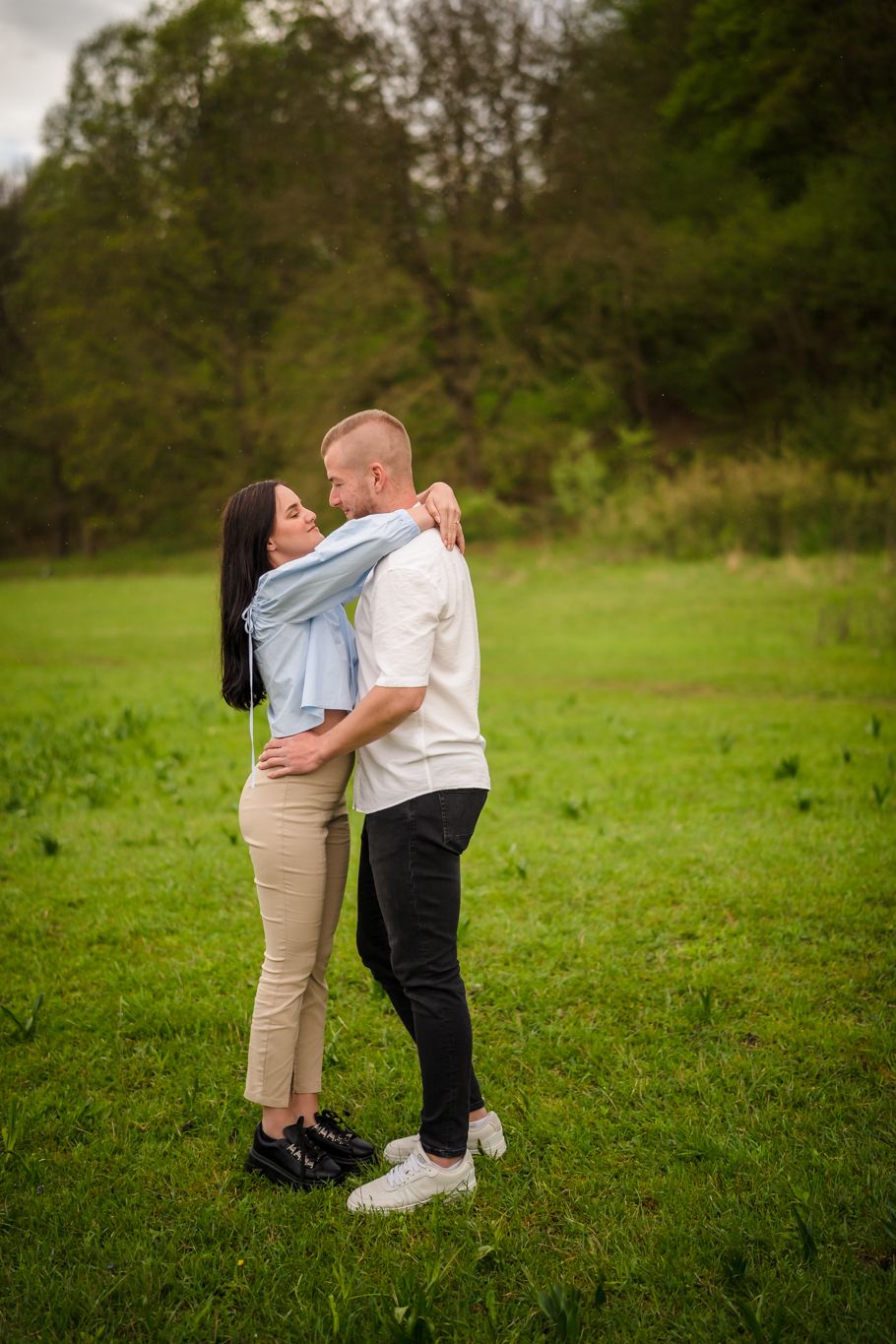Couple sharing an intimate moment on a grassy field with trees in background.