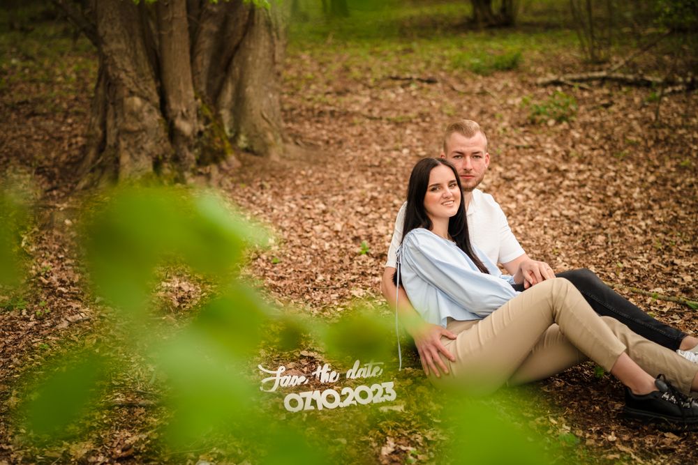 A romantic engagement photoshoot in a wooded forest setting with natural lighting and fallen leaves.