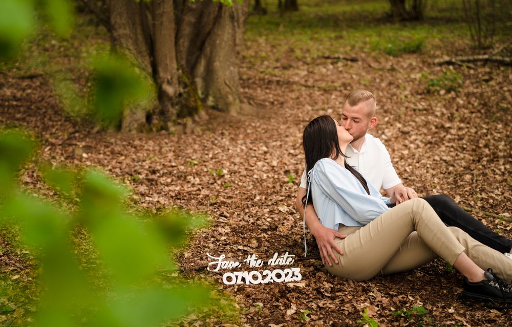 A couple sits together on fallen leaves in a serene forest setting during autumn.