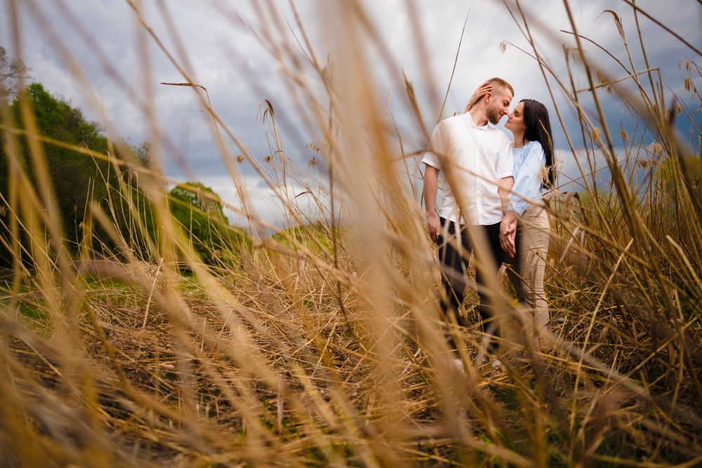 Romantic moment captured through tall grass in golden light.