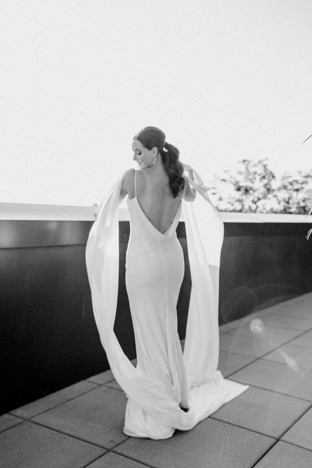 Stunning back view of elegant wedding dress with deep V and flowing train on outdoor terrace.