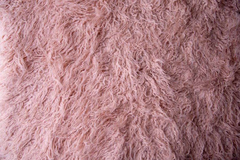 Close-up texture of soft pink curly shaggy fur fabric background.