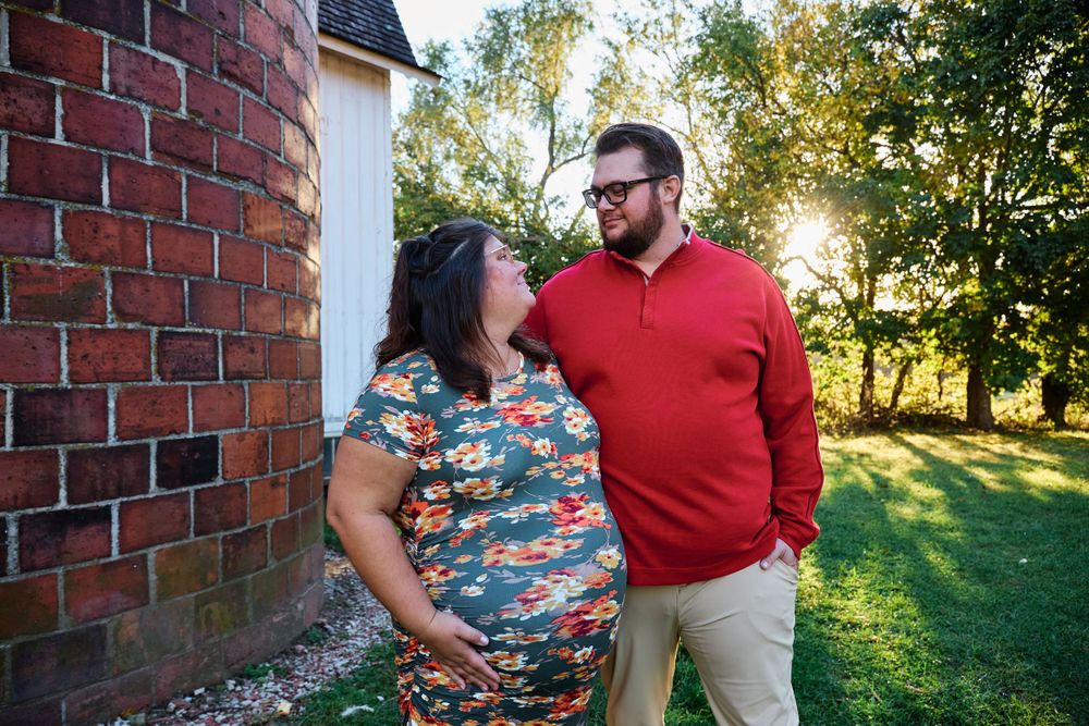 Couple shares an intimate moment outdoors near a brick building during sunset.