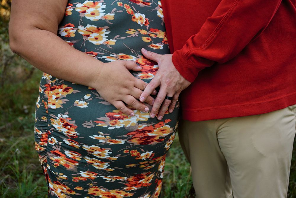 Close-up of hands resting on a floral print maternity dress during an outdoor photoshoot.