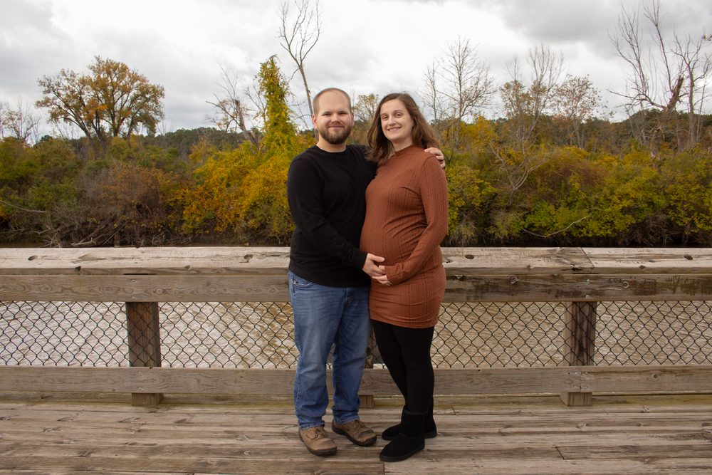 Maternity portrait on wooden bridge with fall colors in background.